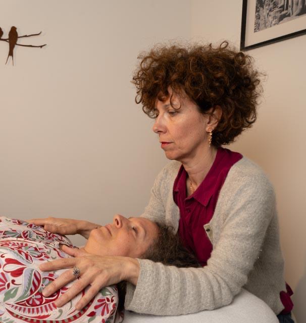 Agnès Barret, les mains posées sur la tête d'une patiente allongée, lors d'une séance de fasciathérapie